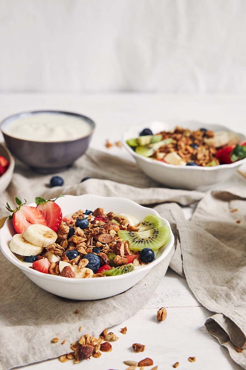 Several bowls of granola with yogurt, fruits and berries on a white surface